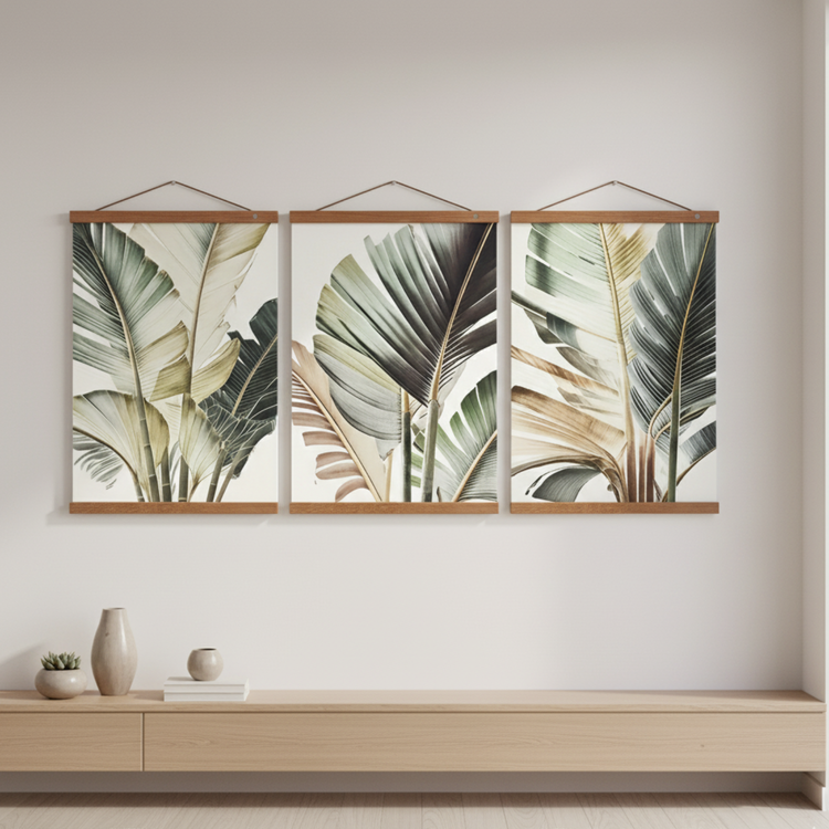 Three botanical wall art prints featuring soft green and beige palm leaves, displayed as a coordinated set with wooden hanging rails frames above a minimalist console table.